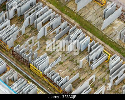 Vista aerea di elementi in cemento precompresso immagazzinati in un cortile industriale con scaffali metallici e chiazze d'erba, Polonia. Foto Stock