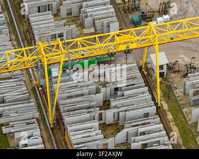 Vista aerea di un cortile di stoccaggio pieno di file di pannelli murali in calcestruzzo precompresso e di una grande gru a portale gialla in Polonia. Foto Stock