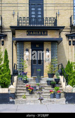 Ingresso dell'edificio dell'hotel Carlyle con porta nera, gradini in pietra, vasi di fiori e balcone in ferro decorativo. Foto Stock