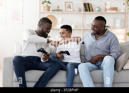 Felice uomo anziano che guarda suo figlio e suo nipote giocare ai videogiochi Foto Stock