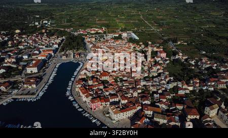 Vista aerea che mostra la città di Stari Grad sull'isola di Hvar, Croazia, con barche ormeggiate nell'antico porto e il paesaggio verde circostante Foto Stock