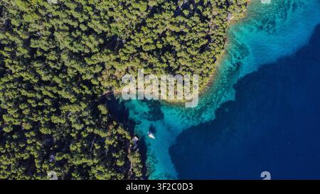 Vista aerea che mostra acqua turchese chiara che incontra una foresta verde e lussureggiante, con una barca che gode della baia calma e isolata Foto Stock