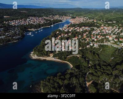 Stari grad che mostra case e un porticciolo lungo una bellissima baia con acqua turchese limpida e natura rigogliosa Foto Stock