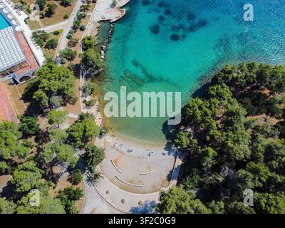 Vista aerea che mostra acqua turchese chiara che bagna dolcemente la spiaggia di ciottoli, circondata da rigogliosi pini verdi sull'isola di Hvar Foto Stock