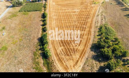 Vista aerea di un campo agricolo raccolto con intricati motivi di tracce lasciate dai trattori, circondato da alberi e paesaggio rurale nel distretto di Srem, Vojvodina Foto Stock