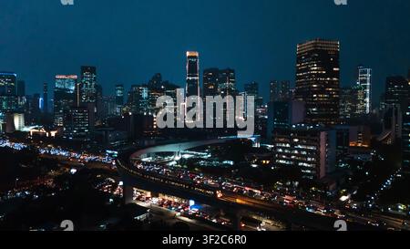 Vista aerea dello skyline illuminato di Jakarta di notte con grattacieli e traffico intenso sull'autostrada sopraelevata a Jakarta, Indonesia. Foto Stock