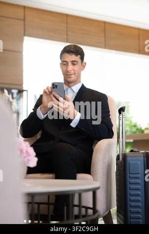 Uomo che utilizza uno smartphone per la comunicazione online nel salone dell'hotel Foto Stock