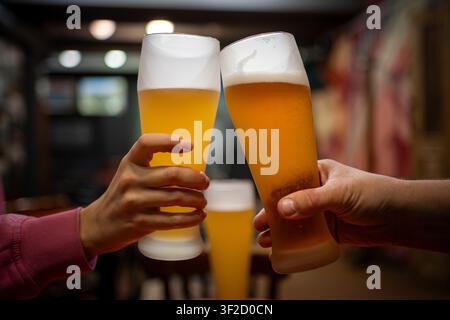 Amici che brindano con bicchieri di birra alla spina in un pub. Primo piano del brindisi con bicchieri di birra ghiacciati, celebrazione, ritrovo sociale, vita notturna, birreria, ristorante Foto Stock