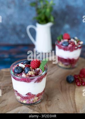 Composizione di styling alimentare con yogurt a strati, frutti di bosco e granola con dessert aggiuntivo sullo sfondo Foto Stock