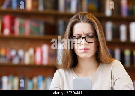 Giovane donna che indossa occhiali seduti in un bar e navigando il suo telefono Foto Stock