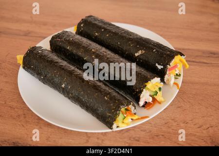 Rotolo di Kimbap fatto in casa su piatto bianco prima del taglio Foto Stock