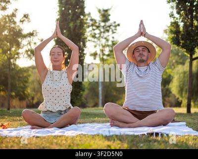 Coppia adulta multirazziale che pratica yoga nel parco in estate. Posizione del loto. Foto Stock