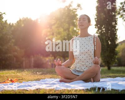 Donna adulta che pratica yoga nel parco in estate. Posizione del loto. Foto Stock