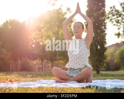 Donna adulta che pratica yoga nel parco in estate. Posizione del loto. Foto Stock