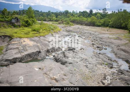 Ampio paesaggio scenografico di un fiume che scorre attraverso un terreno roccioso eroso e colline boschive rigogliose sotto un cielo nuvoloso tropicale Foto Stock