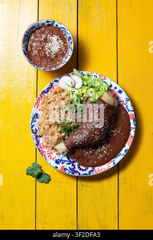 Questo piatto vivace presenta mole poblano versato sulle enchiladas, accompagnato da riso condito e guarnito con lattuga, ravanelli ed erbe fresche, perfetto per un'occasione festiva. Foto Stock