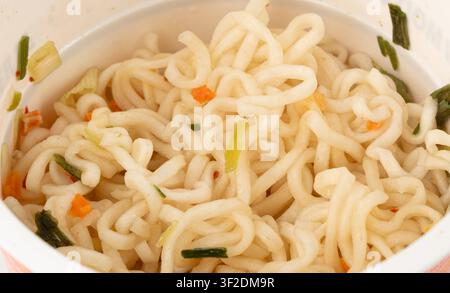 Asciugare gli spaghetti istantanei in una tazza isolata. Spaghetti crudi in acqua calda, pasta fast food in contenitore, confezione aperta con spaghetti di ramen istantanei sul retro bianco Foto Stock