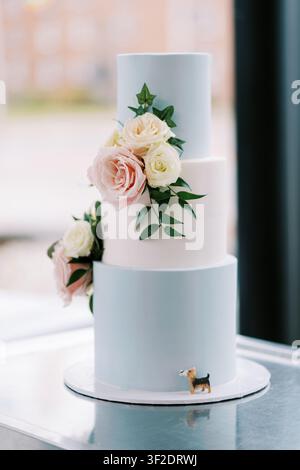 Elegante torta nuziale a tre piani con rose e statuetta di cane Foto Stock