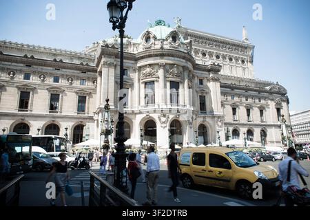 La facciata ornata del Palais Garnier si erge sopra i pedoni e il traffico su una strada cittadina affollata a Parigi, Île-de-France, Francia. Foto Stock