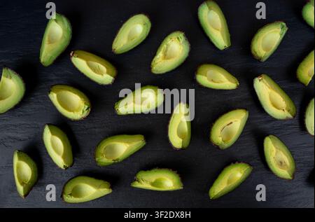 Molte fette di avocado Hass su sfondo nero, motivo di avocado marroni tagliati, pezzi freschi di pera alligatore, ingrediente per guacamole, avocado Persea americana Foto Stock