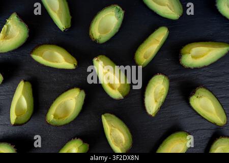 Molte fette di avocado Hass su sfondo nero, motivo di avocado marroni tagliati, pezzi freschi di pera alligatore, ingrediente per guacamole, avocado Persea americana Foto Stock