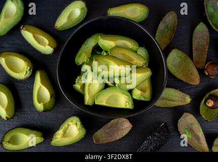 Molte fette di avocado Hass e buccia su sfondo nero, motivo di pezzi di avocado marroni, pezzi freschi di pera alligatore, ingrediente per il compost, Persea Americana Foto Stock