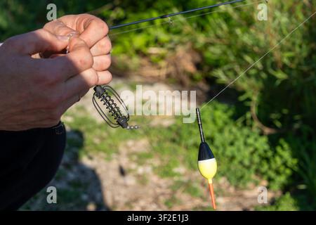 Un primo piano, una prospettiva in prima persona delle mani di un pescatore che prepara un rig a cestino per l'esca. La scena evidenzia il lato tecnico della pesca Foto Stock