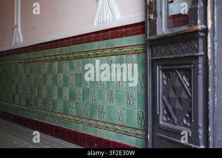 Berlino, Germania - 18 luglio 2026: Dettaglio dell'ingresso interno in stile Art Nouveau con piastrelle verdi ornate, fregio e porta in legno storica a Friedrichshain. Foto Stock