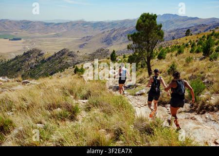 Gruppo di tre donne trail runner che corrono su un sentiero di pietra con una vista panoramica su montagne aride Foto Stock