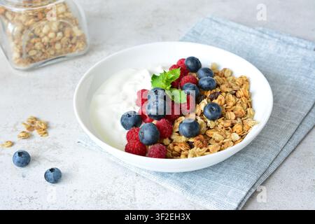 Ciotola di yogurt con granola e mirtilli freschi e lamponi su tavolo con tovagliolo grigio Foto Stock