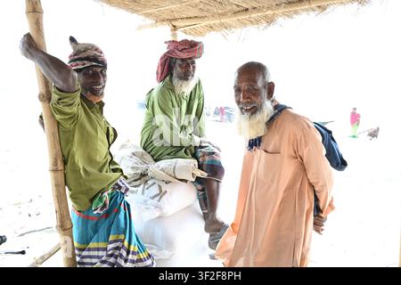 Distretto di Gaibandha, Divisione di Rangpur, Bangladesh – 15 febbraio 2026: Vista di tre uomini anziani in abiti tradizionali che riposano sotto un riparo di bambù Foto Stock