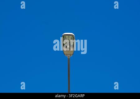 Vista frontale a basso angolo di un moderno lampione pubblico montato su un palo di metallo, perfettamente centrato nell'inquadratura. Il lampione si erge contro un cielo blu Foto Stock