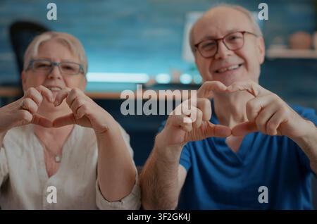 Nonni che formano una forma a cuore con le dita, nonni sposati formano una forma a cuore con le dita, esprimendo affetto, amore e devozione in un ritratto caldo. Foto Stock