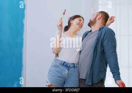 Coppia sposata allegra si diverte durante la ristrutturazione della casa, lavorando insieme alla ridecorazione dell'appartamento, alla costruzione e alle riparazioni in un momento domestico giocoso. Foto Stock
