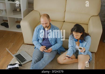 Coppia che si rilassa navigando su internet nel loro accogliente appartamento, con lavoro su laptop e dispositivo digitale, connettendo lavoro su laptop, dispositivo digitale e lavoro su computer. Foto Stock