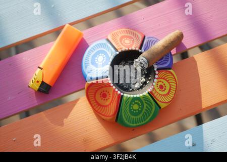 Sigaro appoggiato in un posacenere colorato su tavolo di legno Foto Stock
