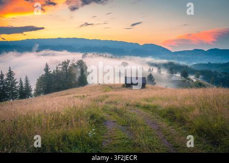 Paesaggio rurale autunnale pittoresco e valle profonda nebbiosa. Vecchie capanne di legno sulle colline nebbiose al tramonto, Carpazi, Transilvania, Romania, Europa Foto Stock