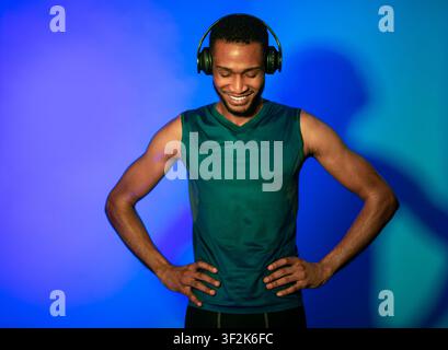 Atleta Man in Fitwear e auricolari in piedi su sfondo blu Foto Stock