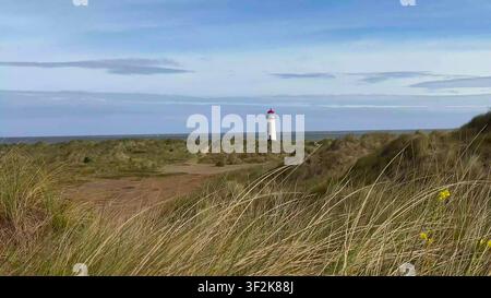 TALACRE, GALLES - 05 LUGLIO 2024: Il faro di Point of Ayr visto da lontano dietro dune sabbiose ed erba alta della spiaggia a Talacre, nel Galles del Nord. Foto Stock