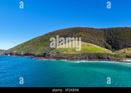 Vista aerea delle acque turchesi limpide che circondano Blueys Head a Blueys Beach, con la scogliera rocciosa, la costa sabbiosa e le acque costiere vibranti Foto Stock