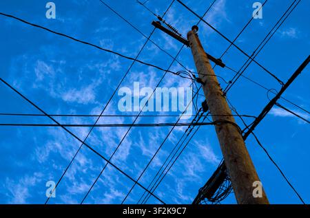 Vista ad angolazione bassa di un palo di servizio in legno con una rete caotica di linee elettriche sullo sfondo di un cielo blu con nuvole sottili a Vancouver, British Columbia Foto Stock