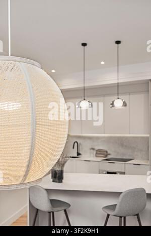 Dettaglio di una lampada a sospensione tessuta con sfondo sfocato di cucina che mostra due lampade a sospensione cromate e sgabelli da bar imbottiti grigi in lontananza. Foto Stock