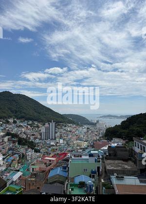 Vista aerea del villaggio culturale di Gamcheon con case colorate a cascata che scendono lungo il pendio verso la baia di Busan, in Corea del Sud, sotto un cielo nuvoloso drammatico Foto Stock