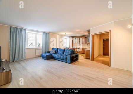 Spazio abitativo luminoso e open plan. Divano angolare blu, pavimenti in legno e una cucina visibile sullo sfondo. Caldo, accogliente e pulito Foto Stock