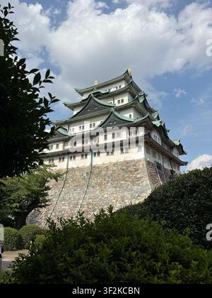 5 agosto 2025, Nagoya, Giappone – I tetti di pagoda iconici con piastrelle verdi del castello di Nagoya visti da un angolo basso attraverso una rigogliosa vegetazione estiva su un cielo blu con nuvole. Foto Stock