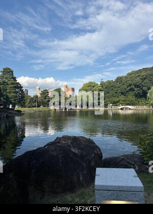 7 agosto 2025, Nagoya, Giappone – Il castello di Nagoya visto attraverso il fossato con rocce da giardino tradizionali e alberi verdi sotto un cielo estivo azzurro. Foto Stock