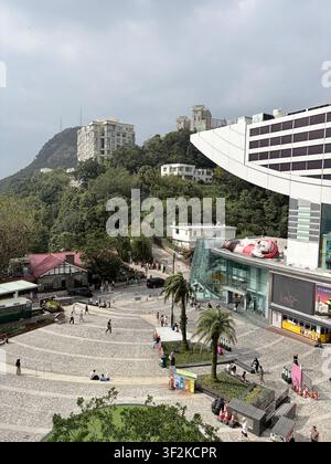 31 ottobre 2025, Hong Kong, Cina – Piazza commerciale della torre Victoria Peak con figura di Topolino, palme e turisti su una passeggiata lastricata. Foto Stock