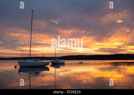 Yacht ancorati su una superficie d'acqua calma del lago che riflette un drammatico cielo dorato all'alba, bella scena portuale mattutina. Foto Stock