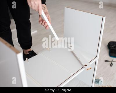 Primo piano di una donna caucasica che assembla a casa una nuova mensola o scrivania in legno bianco sul pavimento, utilizzando attrezzi, concetto di mobili autoassemblati. Foto Stock