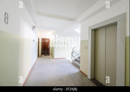 L'immagine mostra una vista interna del corridoio di un edificio residenziale, con un ascensore, una scala e porte d'ingresso. Le pareti sono dipinte in due tonalità Foto Stock